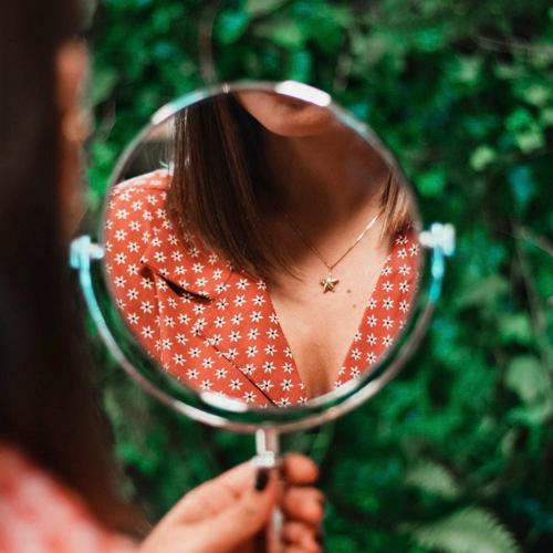 Fille tenant un miroir où seul son torse est reflété, posant avec un pendentif Hissia.